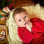baby, infant, red_clothing, blanket, basket, holiday_decor, gingerbread_man, santa_figurine, wooden_table, face, hands, blue_eyes, cozy, cute, festive, christmas, portrait, indoor, soft_texture, curious