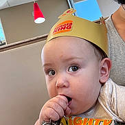 Greyson joined the competition — help win amazing prizes! baby, child, burger_king, paper_crown, keys, hand, face, curious, indoor, restaurant, booth, light, red_light, adult, person, clothing, skin, head, expression, holding