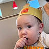 baby, child, burger_king, paper_crown, keys, hand, face, curious, indoor, restaurant, booth, light, red_light, adult, person, clothing, skin, head, expression, holding