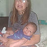 Elijah is registered to the contest to win money with this photo: baby, infant, child, adult, portrait, sitting, lap, glasses, brown_hair, purple_clothing, onesie, white_socks, smiling, indoors, bedroom, bed, blanket, window, blinds, family