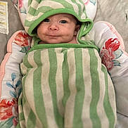 Kehlani is registered to the contest to win money with this photo: baby, infant, striped_towel, green, white, hood, smile, face, cushion, floral, pattern, blanket, cute, child, wrapped, lying_down, soft, comfortable, indoor, portrait
