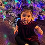 Novalee joined the competition — help win amazing prizes! baby, child, christmas_tree, holiday_lights, indoor, floor, curly_hair, sitting, velvet_dress, black_leggings, white_socks, decorations, festive, cute, portrait, holiday_season, home, colorful_lights, wooden_floor, infant