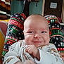 baby, smile, festive_leggings, holiday_pattern, person, indoor, cozy, blanket, door, sign, clothing, face, infant, pattern, hand, sleeve, happy, child, cute, warm