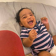 Ameera is registered to the contest to win money with this photo: baby, child, smiling, laughing, curly_hair, striped_clothing, onesie, infant, happy, reclining, indoor, soft_surface, couch, head, face, hand, skin, person, cute, toddler
