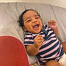 baby, child, couch, curly_hair, cute, face, hand, happy, head, indoor, infant, laughing, onesie, person, reclining, skin, smiling, soft_surface, striped_clothing, toddler