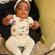 Ameera is registered to the contest to win money with this photo: baby, infant, headband, strawberry_print, white_clothing, carpet, indoor, child, cute, sitting, person, expression, warm_lighting, floor, hand, footwear, apparel, headwear, young_child, portrait