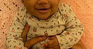 Ameera is registered to the contest to win money with this photo: baby, smiling, infant, hands, knitted_blanket, pink, cute, child, portrait, happy, clothing, long_sleeve, black_pants, curly_hair, skin, person, indoor, holding, young, seated