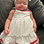 Anahi is registered to the contest to win money with this photo: baby, child, sleeping, headband, dress, white_dress, red_trim, blue_trim, couch, cushion, indoor, peaceful, cute, infant, person, portrait, smile, relaxed, hand, legs