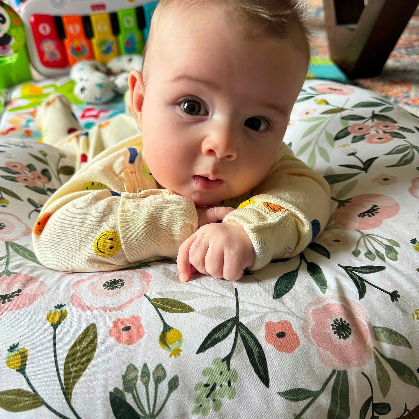 Brooks joined the competition — help win amazing prizes! baby, blanket, child, colorful, couch, curious, expression, eyes, face, floor, floral_pattern, hand, indoor, infant, onesie, pillow, portrait, smiley_face, toy, wooden_floor
