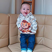 Djeeroy participe au concours pour gagner de l'argent avec cette photo : toddler, child, smiling, hoodie, cartoon, lion, jeans, white_shoes, couch, leather, indoor, furniture, person, happy, standing, sitting_area, shelf, wood, casual_clothing, portrait