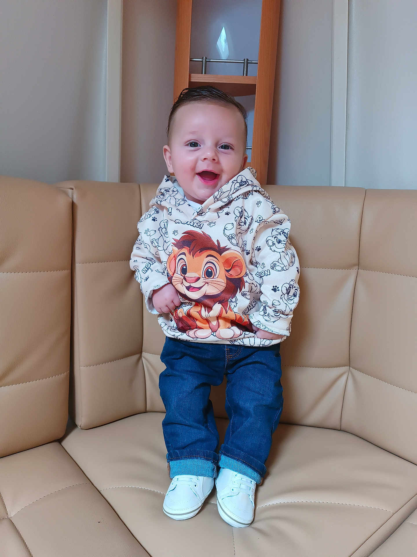 Djeeroy participe au concours pour gagner de l'argent avec cette photo : toddler, child, smiling, hoodie, cartoon, lion, jeans, white_shoes, couch, leather, indoor, furniture, person, happy, standing, sitting_area, shelf, wood, casual_clothing, portrait