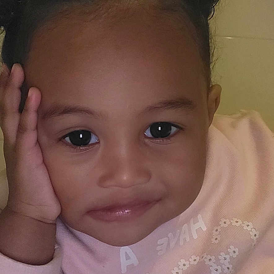 Ioanna a rejoint le concours — aidez-le/la à gagner de superbes lots ! casual, child, closeup, clothing, cozy, curly_hair, cute, expression, face, hair_buns, hand, indoor, person, pink_sweater, portrait, resting_face, smile, tile_wall, toddler, young_child