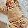newborn, baby, infant, portrait, knitwear, beige_clothing, hat, bear_hat, onesie, sweater, pants, bare_feet, bed, blanket, white_bedding, lying_down, stretching, adorable, cozy, indoor