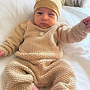 Sylas joined the competition — help win amazing prizes! baby, child, infant, portrait, sitting, lying_down, face, eyes, hat, bear_hat, knitwear, sweater, pants, beige, clothing, bed, blanket, indoor, curtains, cozy
