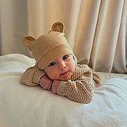 Sylas joined the competition — help win amazing prizes! baby, infant, child, portrait, smiling, face, eyes, bear_hat, knitwear, sweater, beige, cozy, bed, bedding, curtains, indoor, warm_lighting, lying_down, cute, photography