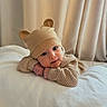 baby, infant, child, portrait, smiling, face, eyes, bear_hat, knitwear, sweater, beige, cozy, bed, bedding, curtains, indoor, warm_lighting, lying_down, cute, photography