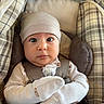 baby, infant, child, portrait, face, wide_eyes, looking_at_camera, car_seat, padded_seat, plaid, blanket, winter_clothing, hat, mittens, onesie, sitting, indoors, cozy, neutral_colors, photography