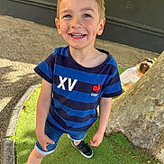 Noah a rejoint le concours — aidez-le/la à gagner de superbes lots ! child, boy, smiling, outdoor, grass, tree, casual_clothing, shorts, black_shoes, blue_shirt, happy, playful, daylight, nature, person, young, posing, background_child, sunlight, recreation