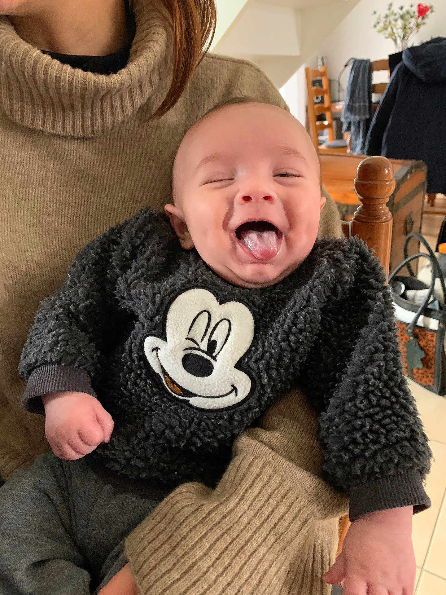 Noah a rejoint le concours — aidez-le/la à gagner de superbes lots ! baby, child, infant, smiling, tongue_out, sweater, mickey_mouse, black_clothing, adult, holding, indoor, home, kitchen, wooden_chair, person, happy, cute, cozy, warm_clothing, portrait