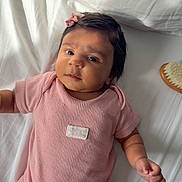 Meera joined the competition — help win amazing prizes! baby, bed, bow, brush, child, cute, expression, face, hair_accessory, hand, indoors, infant, lying_down, newborn, pillow, pink_onesie, portrait, skin, soft_light, white_bed_sheet