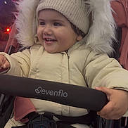 Alaia is registered to the contest to win money with this photo: toddler, child, smiling, winter_clothing, hat, stroller, jacket, baby, happy, outdoor, night, holiday_lights, fur_hood, warm_clothes, person, seatbelt, cute, portrait, festive, seasonal