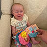 Eleanor is registered to the contest to win money with this photo: baby, infant, child, smiling, happy, portrait, sitting, couch, cushion, indoor, toy, book, colorful, bow, clothing, barefoot, hand, adult_hand, reading, cozy