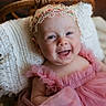 baby, infant, child, smiling, portrait, close_up, flower_crown, pink_dress, ruffles, cushion, blanket, chair, indoor, cozy, happy, face, eyes, photography, soft_lighting, adorable
