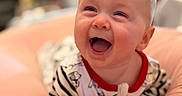 Eleanor is registered to the contest to win money with this photo: baby, infant, child, smiling, laughing, portrait, close_up, indoor, cushion, soft_furnishing, striped_clothing, onesie, red_trim, seated, happy, joyful, face, hands, blurred_background, photography