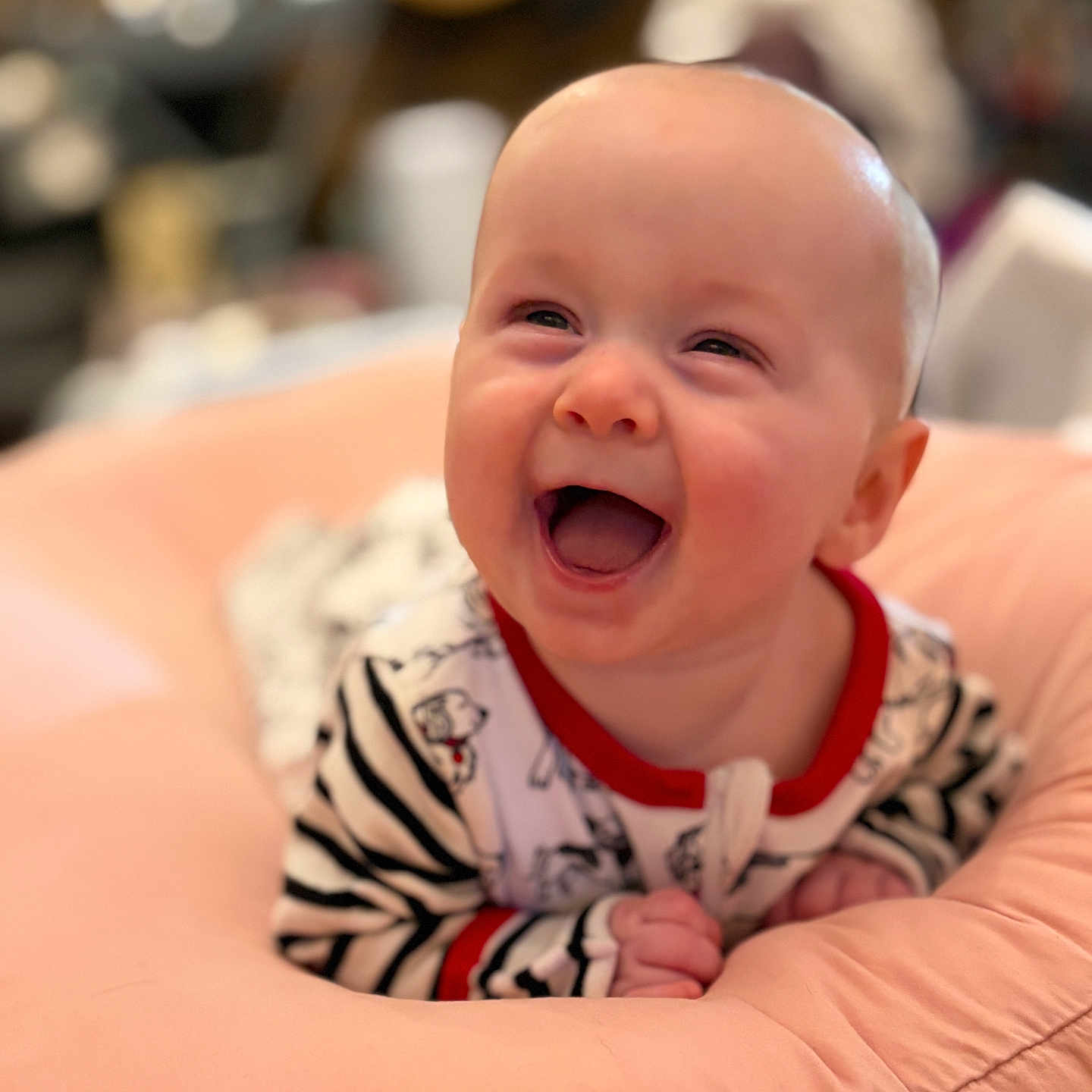 Eleanor is registered to the contest to win money with this photo: baby, infant, child, smiling, laughing, portrait, close_up, indoor, cushion, soft_furnishing, striped_clothing, onesie, red_trim, seated, happy, joyful, face, hands, blurred_background, photography