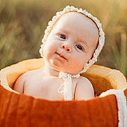 Eleanor joined the competition — help win amazing prizes! baby, infant, child, portrait, sitting, basket, bonnet, frilly, orange, outdoor, blurred_background, close_up, face, eyes, serious_expression, cute, baby_photography, soft_lighting, warm_tones, textile