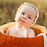 baby, infant, child, portrait, sitting, basket, bonnet, frilly, orange, outdoor, blurred_background, close_up, face, eyes, serious_expression, cute, baby_photography, soft_lighting, warm_tones, textile