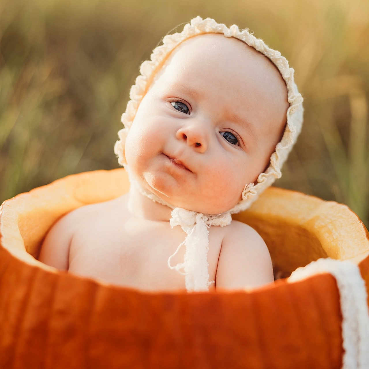 Eleanor joined the competition — help win amazing prizes! baby, infant, child, portrait, sitting, basket, bonnet, frilly, orange, outdoor, blurred_background, close_up, face, eyes, serious_expression, cute, baby_photography, soft_lighting, warm_tones, textile