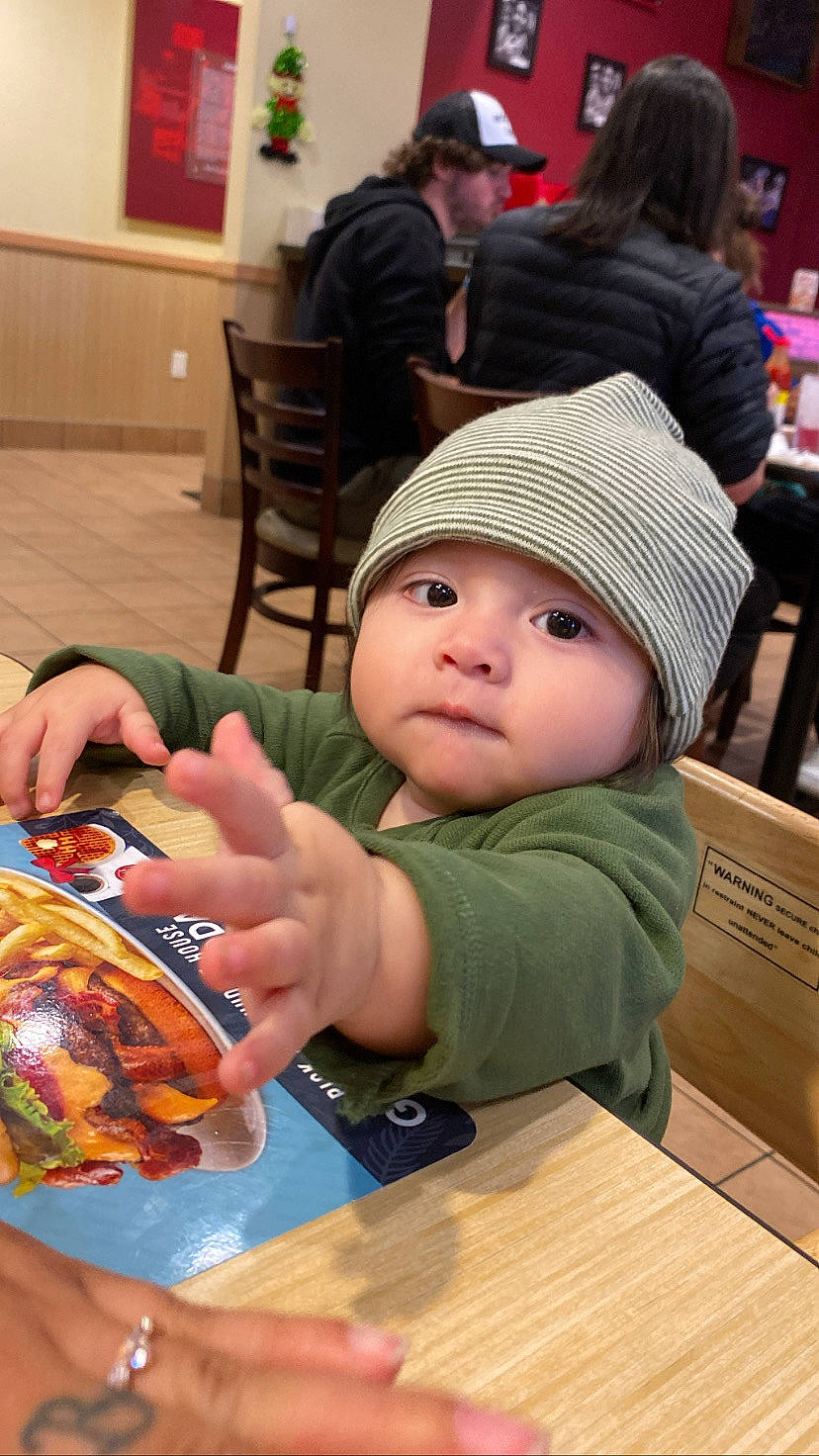 Santiago is registered to the contest to win money with this photo: baby, cap, chair, child, comfort_food, finger_food, fun, headwear, houseplant, junk_food, leisure, nail, person, recreation, room, sharing, sitting, table, tableware, toddler