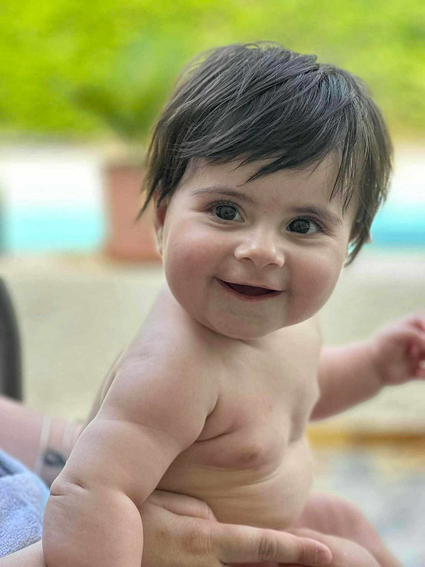 Théa a rejoint le concours — aidez-le/la à gagner de superbes lots ! baby, child, smile, face, skin, dark_hair, bare_shoulders, arm, hand, outdoor, greenery, blurred_background, person, happy, cute, infant, portrait, young_child, closeup, holding