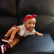 Zoei is registered to the contest to win money with this photo: baby, child, toddler, sitting, couch, portrait, smiling, tongue_out, headband, red_clothing, white_shirt, sneakers, black_couch, indoors, furniture, fashion, cute, casual, infant, photography