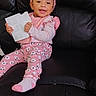 baby, child, infant, smiling, portrait, pink_outfit, floral_clothing, headband, sitting, leather_chair, paper, holding_paper, indoor, close_up, happy, face, earrings, socks, fashion, family_photo