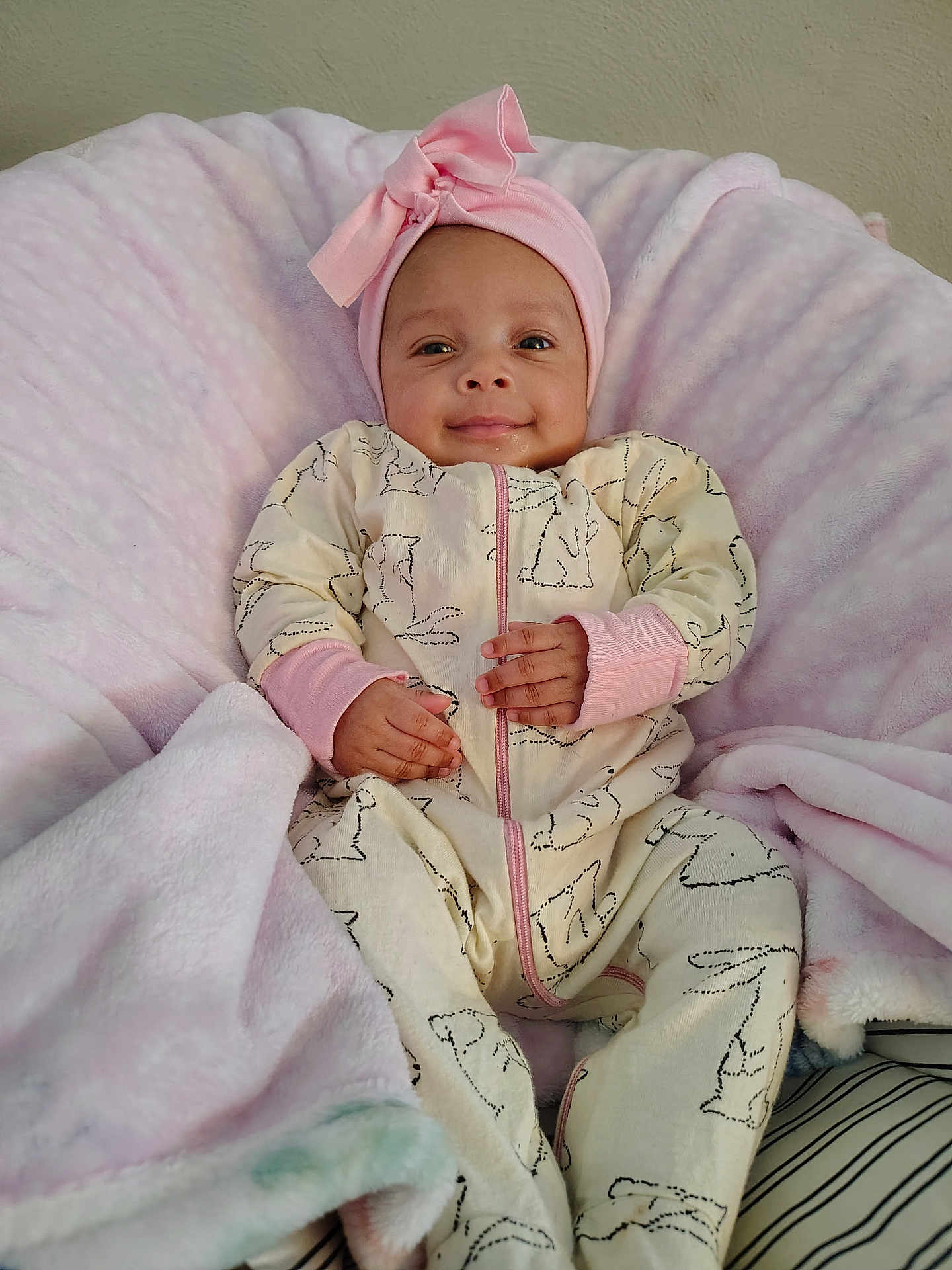 Zoei Zuliana is registered to the contest to win money with this photo: baby, infant, smiling, headband, bow, pink, blanket, onesie, patterned_clothing, zipper, hands, cozy, plush, soft, lying_down, portrait, eyes_open, cheeks, wall, tiny_person