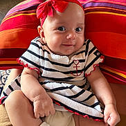 Alicia participe au concours pour gagner de l'argent avec cette photo : baby, child, smile, red_bow, striped_dress, anchor_emblem, sitting, cushion, colorful, indoor, cute, adorable, happy, face, headband, infant, clothing, person, legs, hands