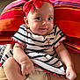 baby, child, smile, red_bow, striped_dress, anchor_emblem, sitting, cushion, colorful, indoor, cute, adorable, happy, face, headband, infant, clothing, person, legs, hands