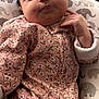 baby, sleeping, onesie, pink, floral_pattern, cushion, elephant_print, infant, cute, cozy, hand, face, closed_eyes, newborn, soft_lighting, indoors, resting, child, portrait, peaceful
