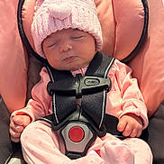 Delilah is registered to the contest to win money with this photo: baby, infant, sleeping, pink_hat, pom_pom, car_seat, safety_harness, pink_outfit, cozy, cute, child, newborn, soft_lighting, indoor, peaceful, closed_eyes, small_hands, footed_pajamas, knit_hat, seat