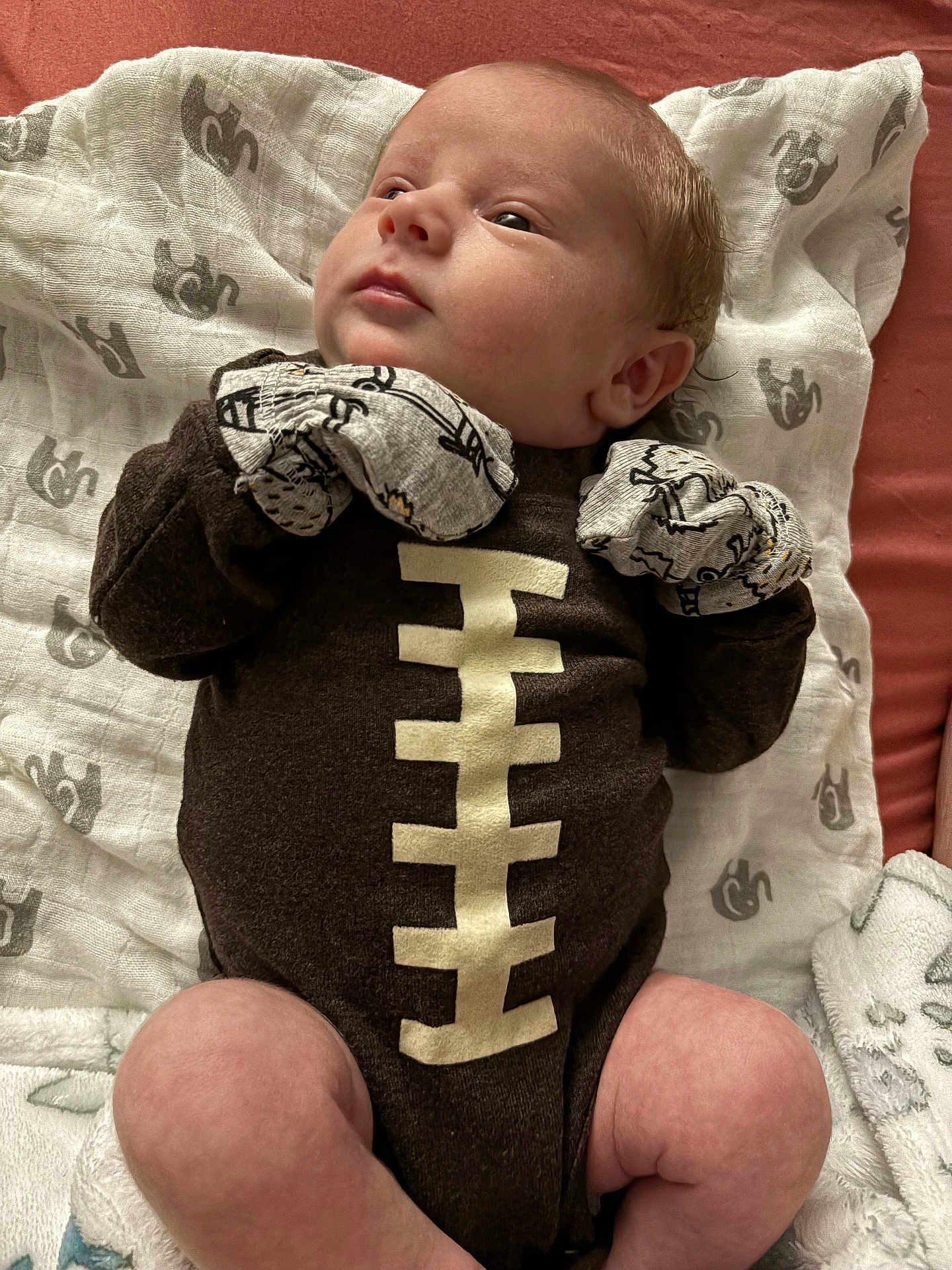 Jaxon joined the competition — help win amazing prizes! baby, infant, newborn, onesie, football_theme, mittens, blanket, lying_down, soft_fabric, cute, child, face, head, skin, sleepwear, indoors, portrait, young_child, cozy, resting