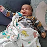 Elijah joined the competition — help win amazing prizes! baby, infant, child, smiling, sleeping, portrait, sitting, couch, cushion, blanket, camouflage_clothing, onesie, toy, indoor, home, cozy, relaxed, face, baby_bottle_clip, text_on_clothing