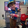 child, costume, police, dog, toy, smile, indoor, television, furniture, clutter, room, floor, sock, plastic_drawer, wall, power_outlet, person, clothing, headwear, play