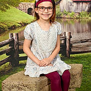Everli Rose is registered to the contest to win money with this photo: child, girl, glasses, headband, flower, dress, leggings, bench, fence, pond, water, grass, trees, building, countryside, smile, outdoor, nature, portrait, happy