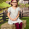 child, girl, glasses, headband, flower, dress, leggings, bench, fence, pond, water, grass, trees, building, countryside, smile, outdoor, nature, portrait, happy