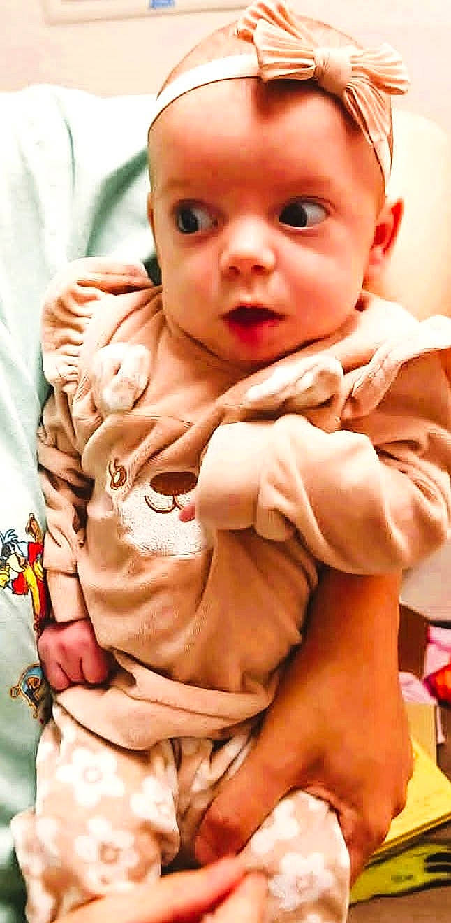 Lilah Jane is registered to the contest to win money with this photo: baby, bow, child, clothing, cozy, curious, cute, expression, hand, headband, holding, indoor, infant, patterned_pants, person, portrait, soft_tones, warm, wide_eyes, young