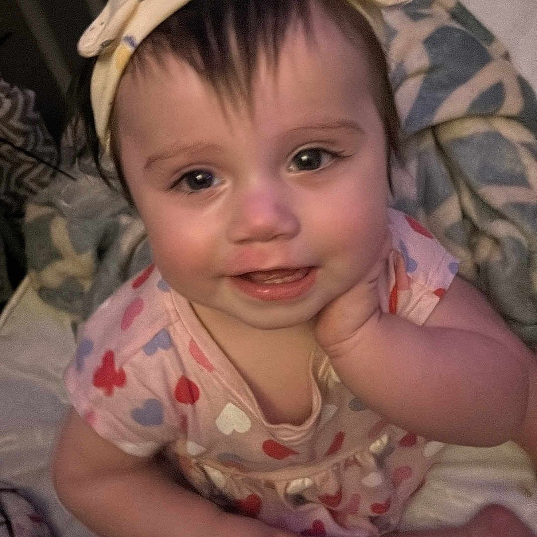 Zoe is registered to the contest to win money with this photo: baby, bed, bonnet, clothing, couch, crib, cushion, dress, face, furniture, happy, hat, head, homedecor, infantbed, person, photography, portrait, sitting, smile