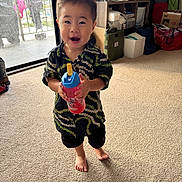 Koa is registered to the contest to win money with this photo: toddler, child, indoor, carpet, barefoot, sippy_cup, smiling, short_hair, shirt, shorts, window, laundry, shelf, storage, box, toy, home, person, happy, daylight