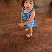 Koa is registered to the contest to win money with this photo: child, barefoot, blue_tank_top, standing, wooden_floor, indoors, curious_expression, toddler, hair, person, floor, toy, casual_clothing, looking_up, young_child, home, skin, face, solemn, standing_barefoot